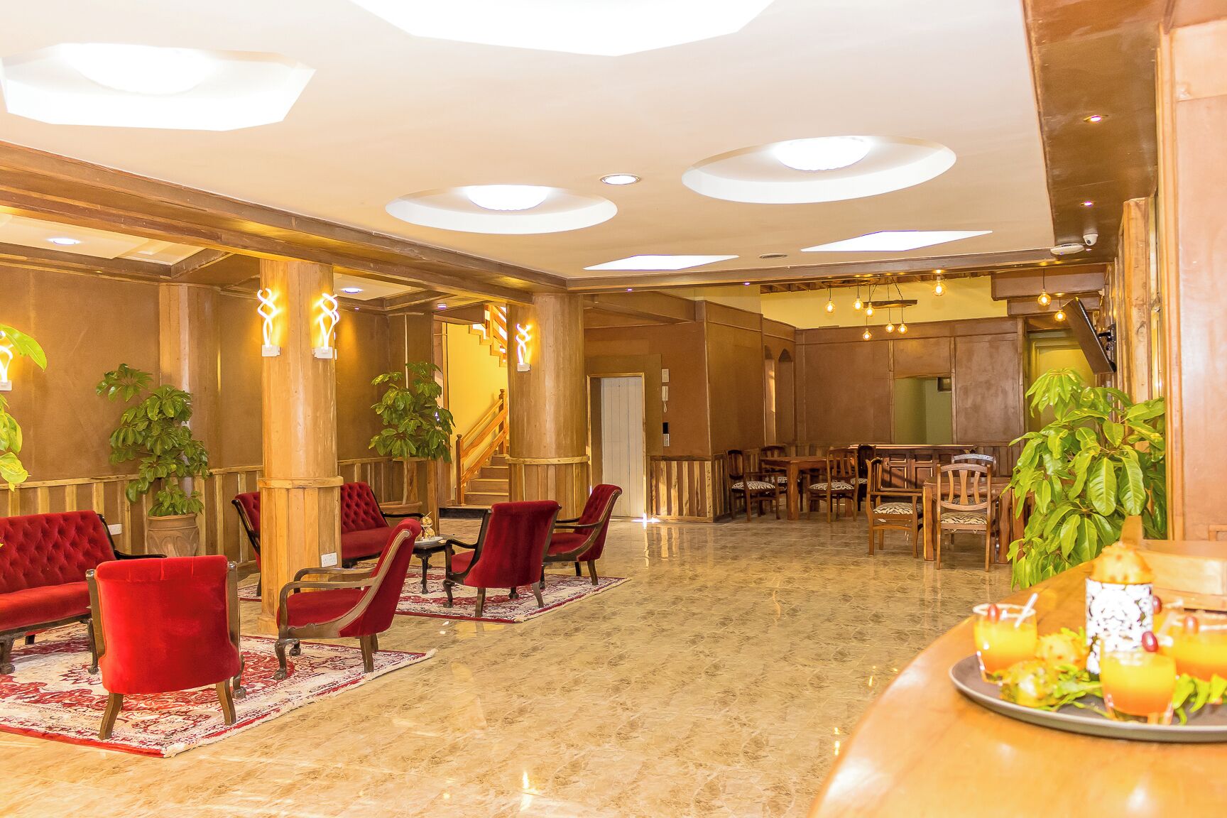 Un hall d’hôtel avec des fauteuils à revêtement rouge, un sol en marbre et un espace repas doté de tables et de chaises en bois.