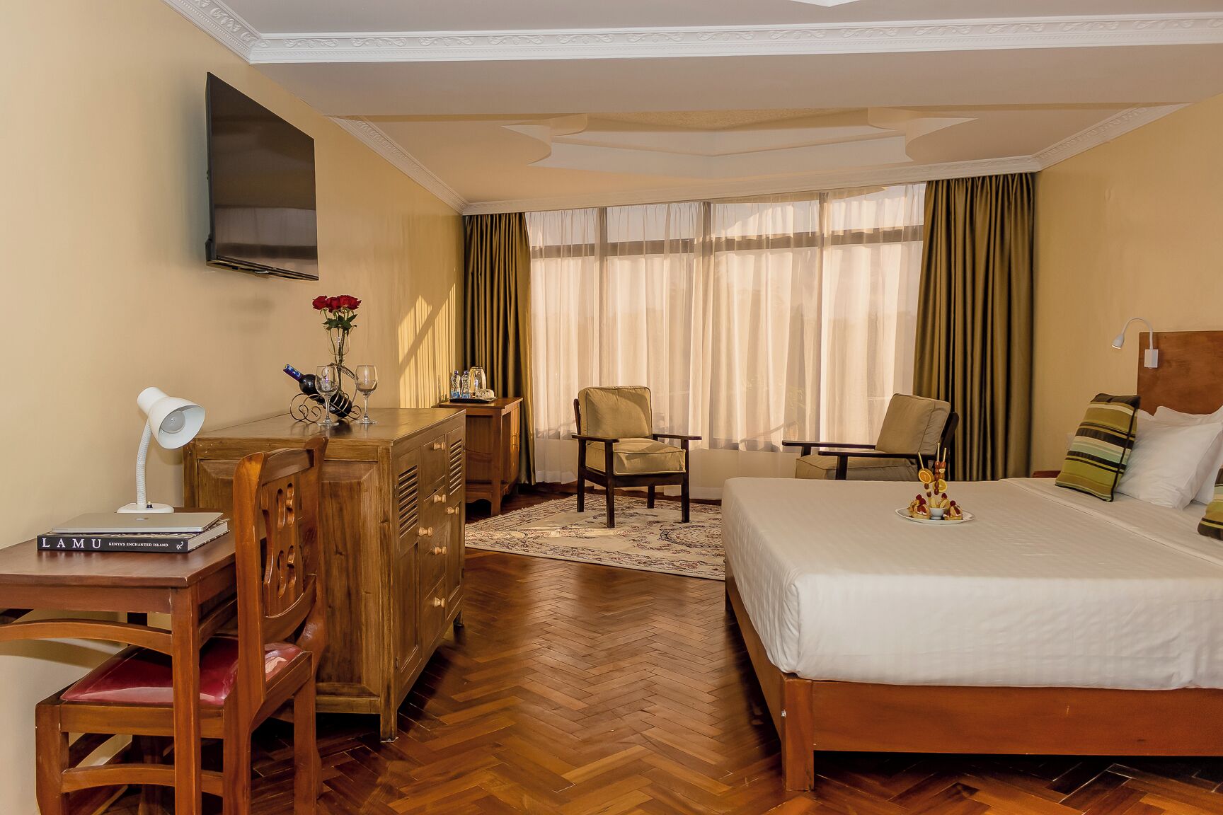 Habitación de hotel con cama, escritorio, sillas, televisor y ventana con cortinas.