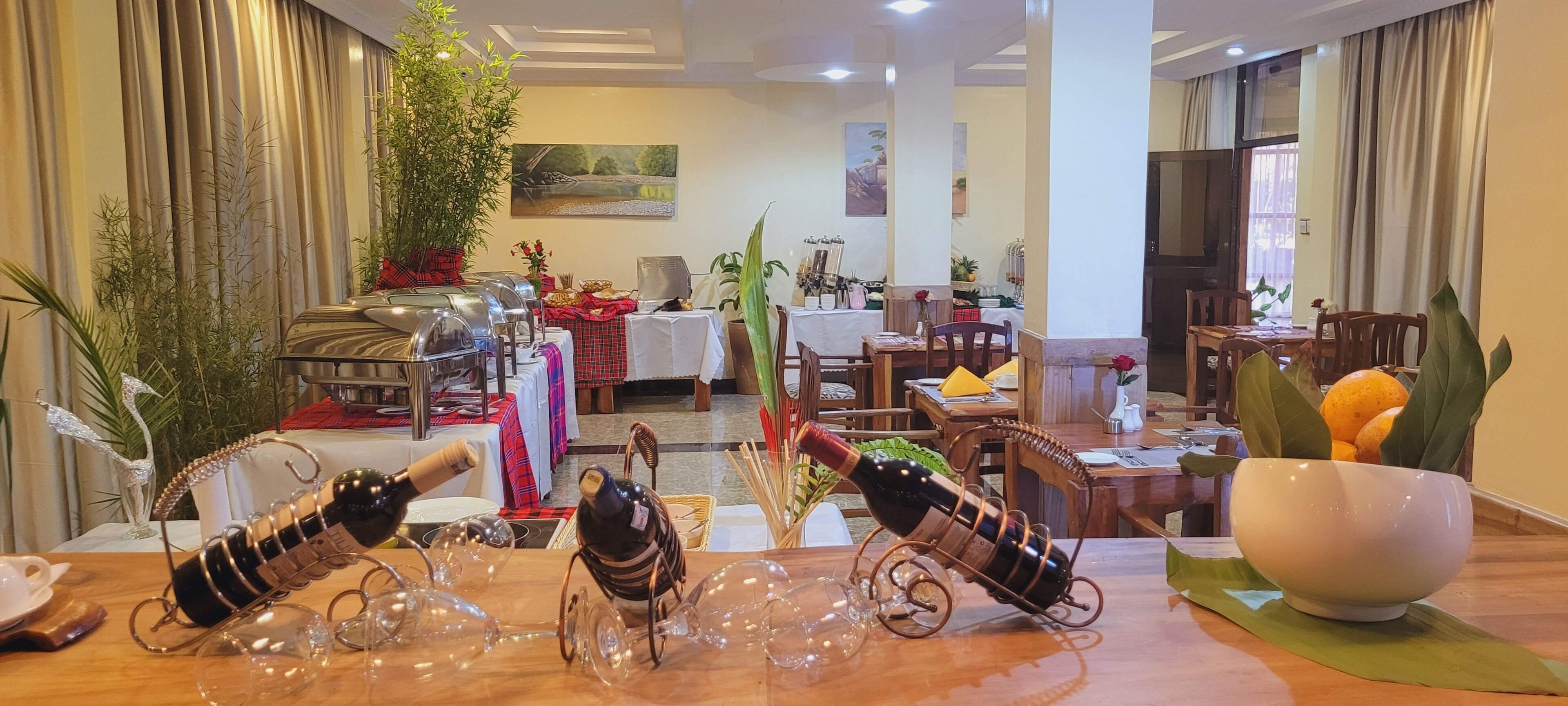 A hotel dining area with tables set for meals, a wine rack, and a large window with curtains.