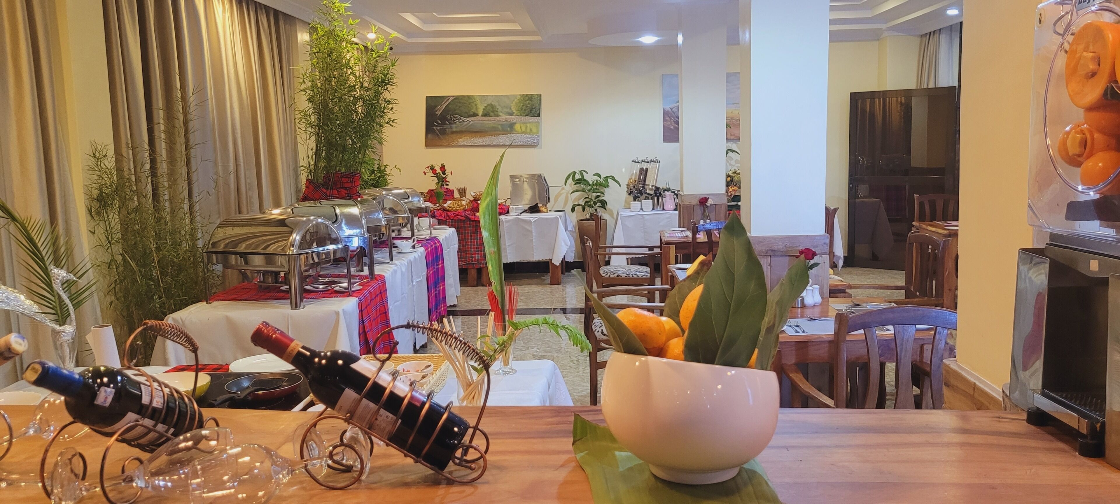 A dining area with tables set for a meal, a buffet with food and drinks, and a large plant in the center.