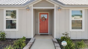 A single-story house with a red door, white siding, and a metal roof.