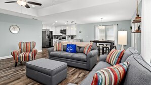 A modern living room with grey sofas, striped armchairs, and a wooden floor.