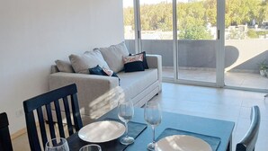 A modern living room with a sofa, dining table set with plates and wine glasses, and a balcony with a view of trees and buildings. - Apartment in the center with a beautiful view of the city (mendoza)