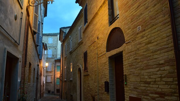 A narrow cobblestone street flanked by historic buildings with arched doorways and traditional shutters. - Residenza Aurea (Offida)