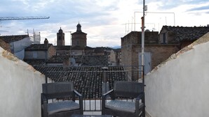 A rooftop terrace with two chairs, a table, and a view of historic buildings and a tower. - Residenza Aurea (Offida)
