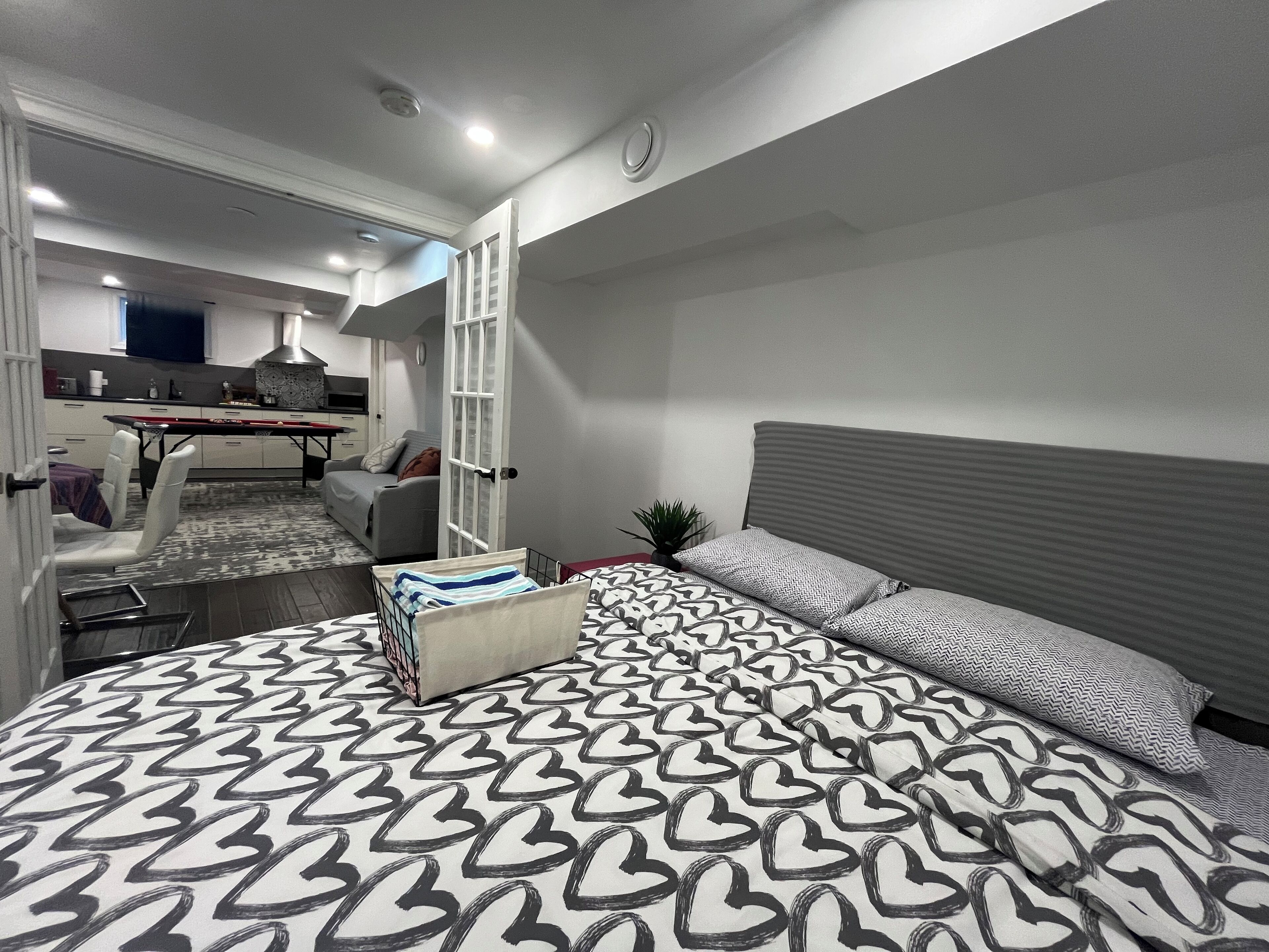 A modern bedroom with a large bed, a bedside table, and a view into the adjacent living area.