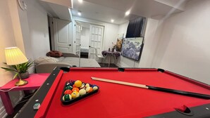Una mesa de billar con bolas, una lámpara y una planta en maceta en una habitación con una cama y un cuadro en la pared.