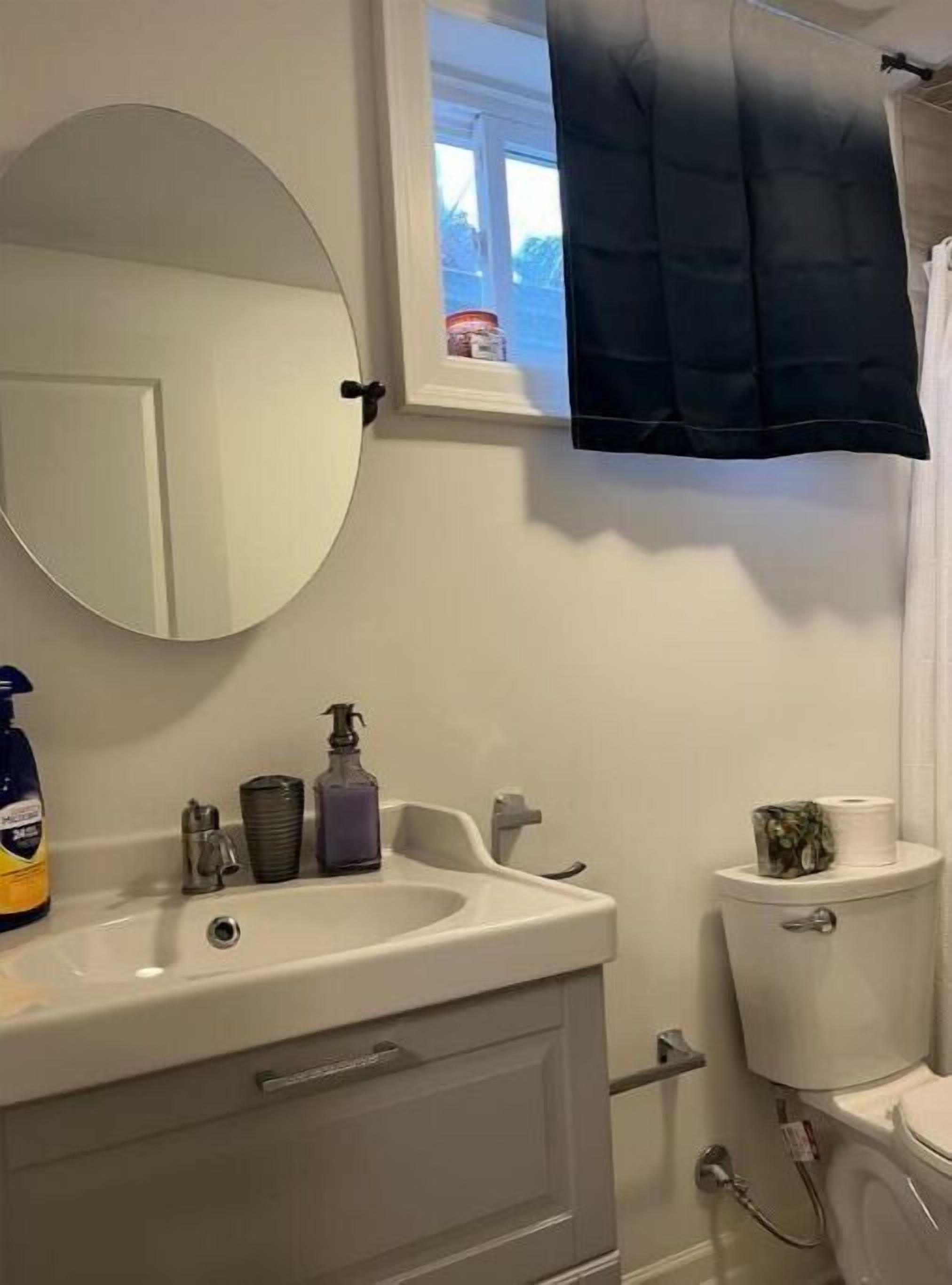 A bathroom with a white sink, mirror, and toilet. There is a window with a towel hanging on the outside.