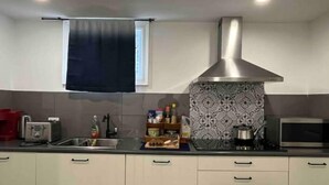 Una cocina moderna con armarios blancos, una campana extractora de acero inoxidable, un salpicadero con diseño y un ventanal con cortina oscura.