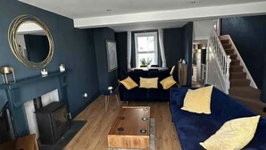 Un salon avec un canapé bleu foncé, une table basse en bois, une cheminée et un escalier.