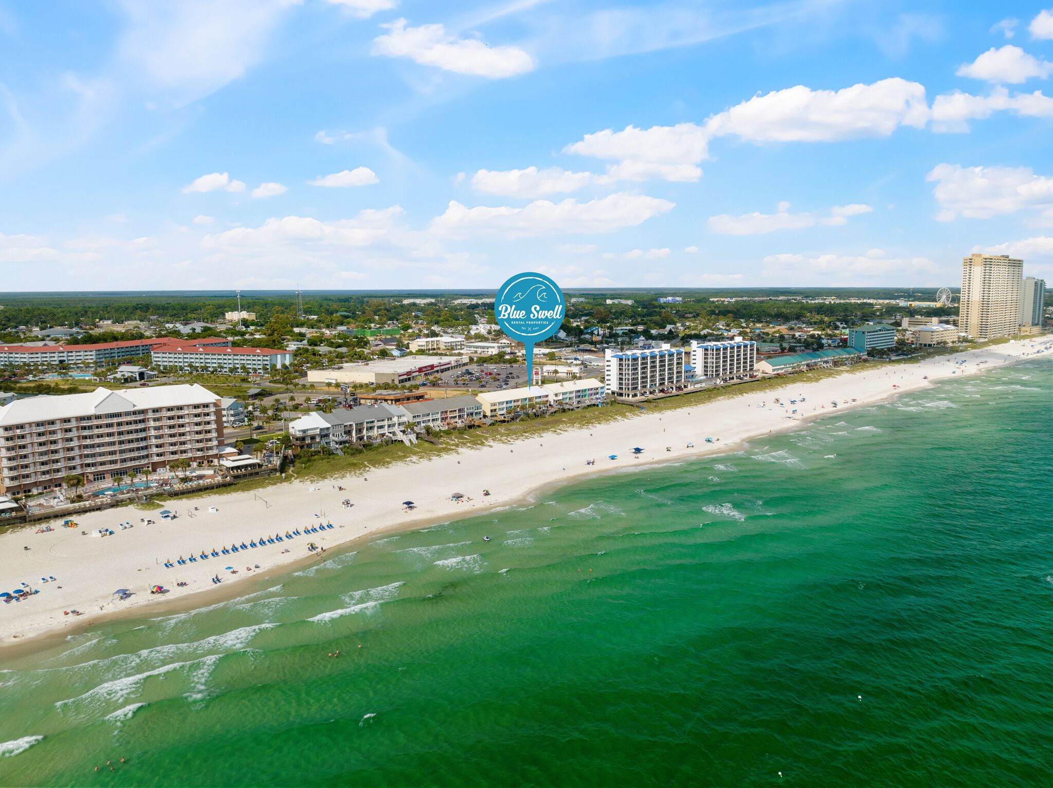 An aerial view of a coastal hotel area with multiple buildings, a beach, and a clear sky.