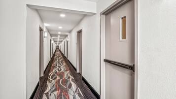Um corredor comprido e estreito, com carpete estampado, paredes brancas e portas em ambos os lados.
