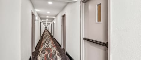 Un long couloir étroit, doté d’un tapis à motifs, de murs blancs et de portes de part et d’autre.