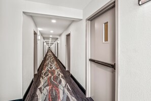 A long, narrow hallway with patterned carpet, white walls, and doors on both sides. - HomeTowne Studios by Red Roof Southfield (Southfield)