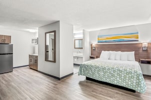 Una habitación de hotel moderna con una cama, una kitchenette pequeña, un baño y un ventanal grande.