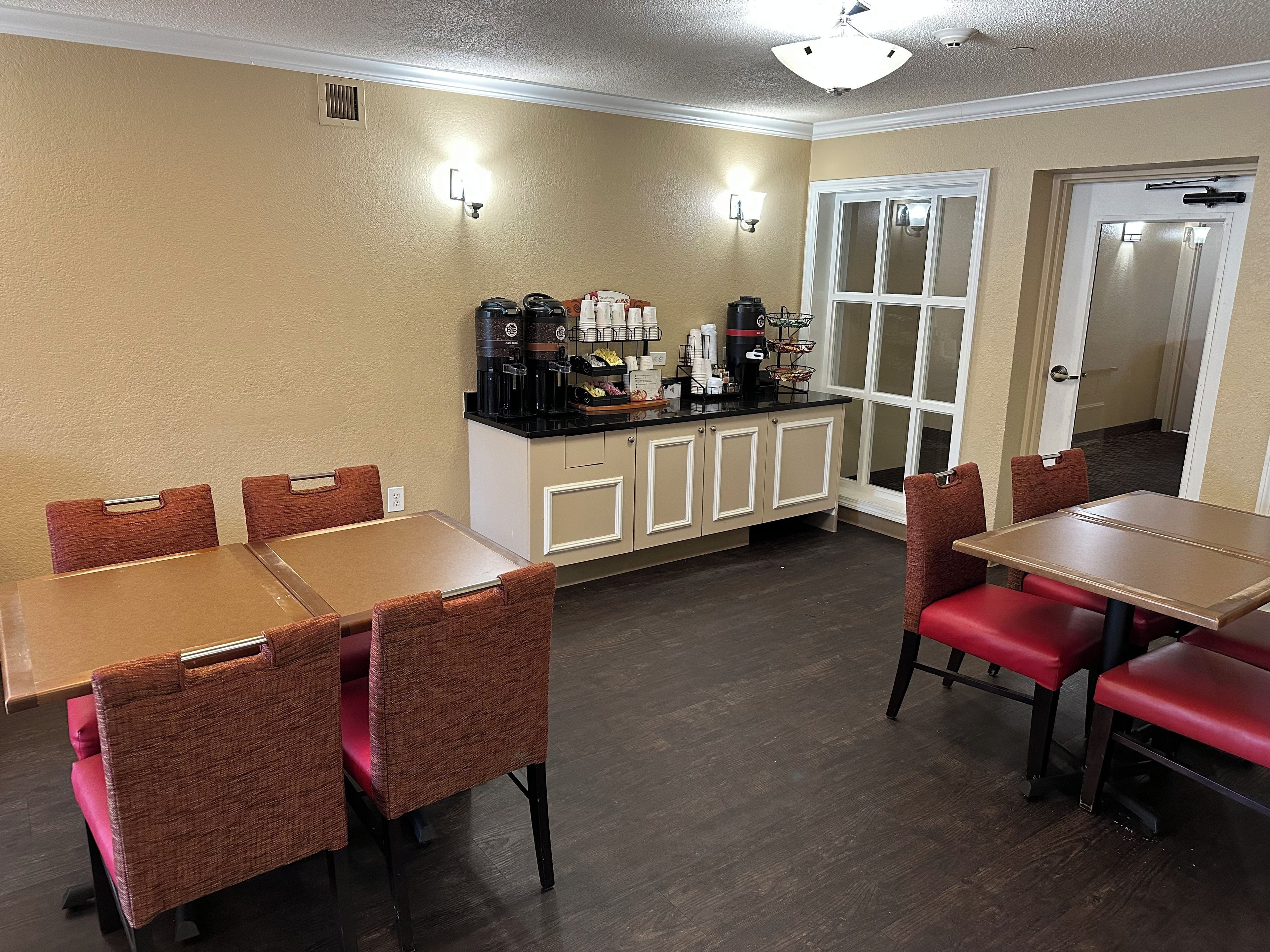 A dining area with tables and chairs, a coffee station, and a door leading to another room.