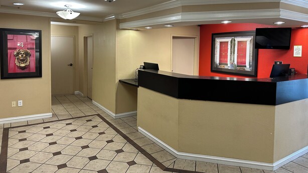 A hotel reception area with a reception desk, a framed welcome sign, and a door. - HomeTowne Studios by Red Roof Southfield (Southfield)