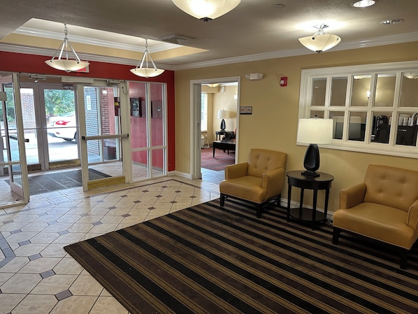 Un hall de hotel con una zona de recepción, dos sillones, una lámpara y una alfombra estampada.