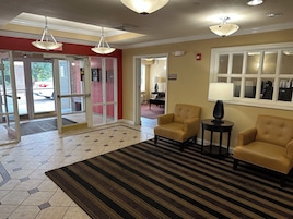 Un hall de hotel con una zona de recepción, dos sillones, una lámpara y una alfombra estampada.