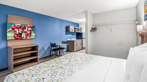 A hotel room with a bed, a TV mounted on the wall, a desk with a chair, a microwave, and a wardrobe. - HomeTowne Studios by Red Roof Southfield (Southfield)