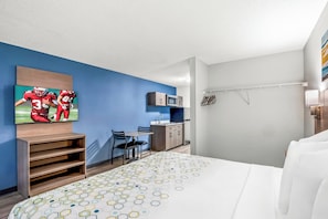 A hotel room with a bed, a TV mounted on the wall, a desk with a chair, a microwave, and a wardrobe. - HomeTowne Studios by Red Roof Southfield (Southfield)