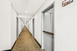 A long, narrow hotel corridor with a patterned carpet, white walls, and doors on both sides. - HomeTowne Studios by Red Roof Southfield (Southfield)
