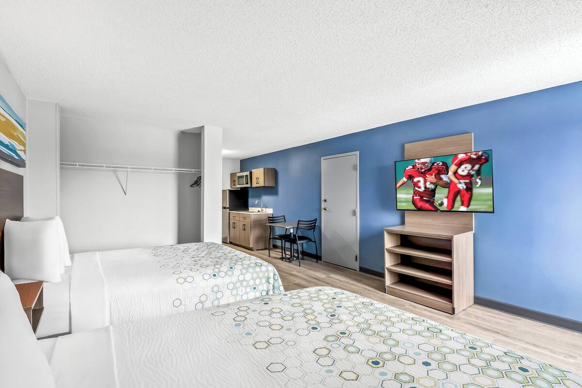 A hotel room with two beds, a TV, a desk, and a microwave.