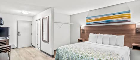A hotel room with a large bed, a desk, a TV, and a bathroom with a mirror and towel rack.