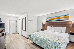 Habitación de hotel con una cama grande, un escritorio, un televisor y un baño con espejo y toallero.