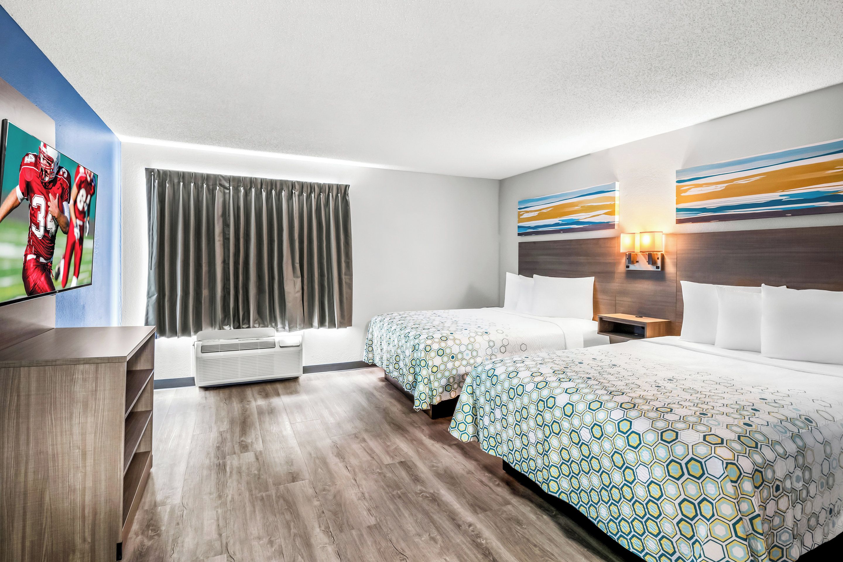 A hotel room with two beds, a TV, a large window with curtains, and a wall with a geometric pattern.
