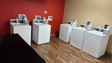 A laundry room with four washing machines, a black table, and a red wall.