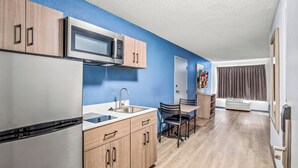 A modern kitchen with wooden cabinets, a stainless steel refrigerator, a microwave, and a sink. - HomeTowne Studios by Red Roof Southfield (Southfield)