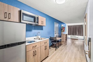 A modern kitchen with wooden cabinets, a stainless steel refrigerator, a microwave, and a sink. - HomeTowne Studios by Red Roof Southfield (Southfield)