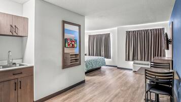 Een moderne hotelkamer met een houten vloer, een bed met een decoratief sprei, een bureau met stoel, een aan de muur bevestigde televisie en een raam met gordijnen.
