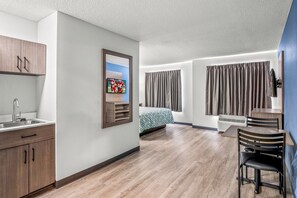 Una habitación de hotel moderna con piso de madera, una cama con cubrecama estampado, un escritorio con silla, un televisor montado en la pared y una ventana con cortinas.