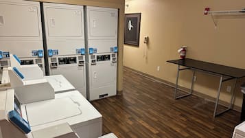 A laundry room with multiple washing machines, a fire extinguisher, and a clock on the wall.