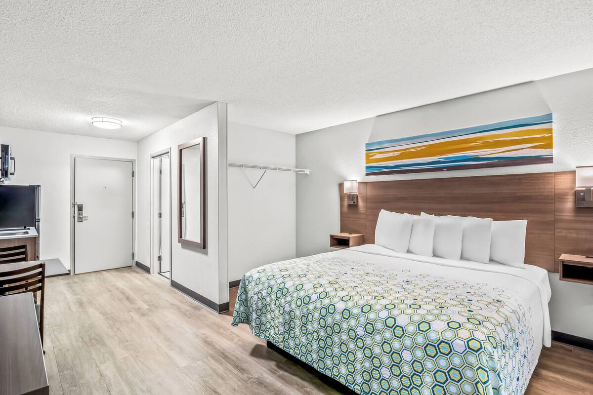 A hotel room with a large bed, a desk, a TV, and a bathroom with a mirror and towel rack.