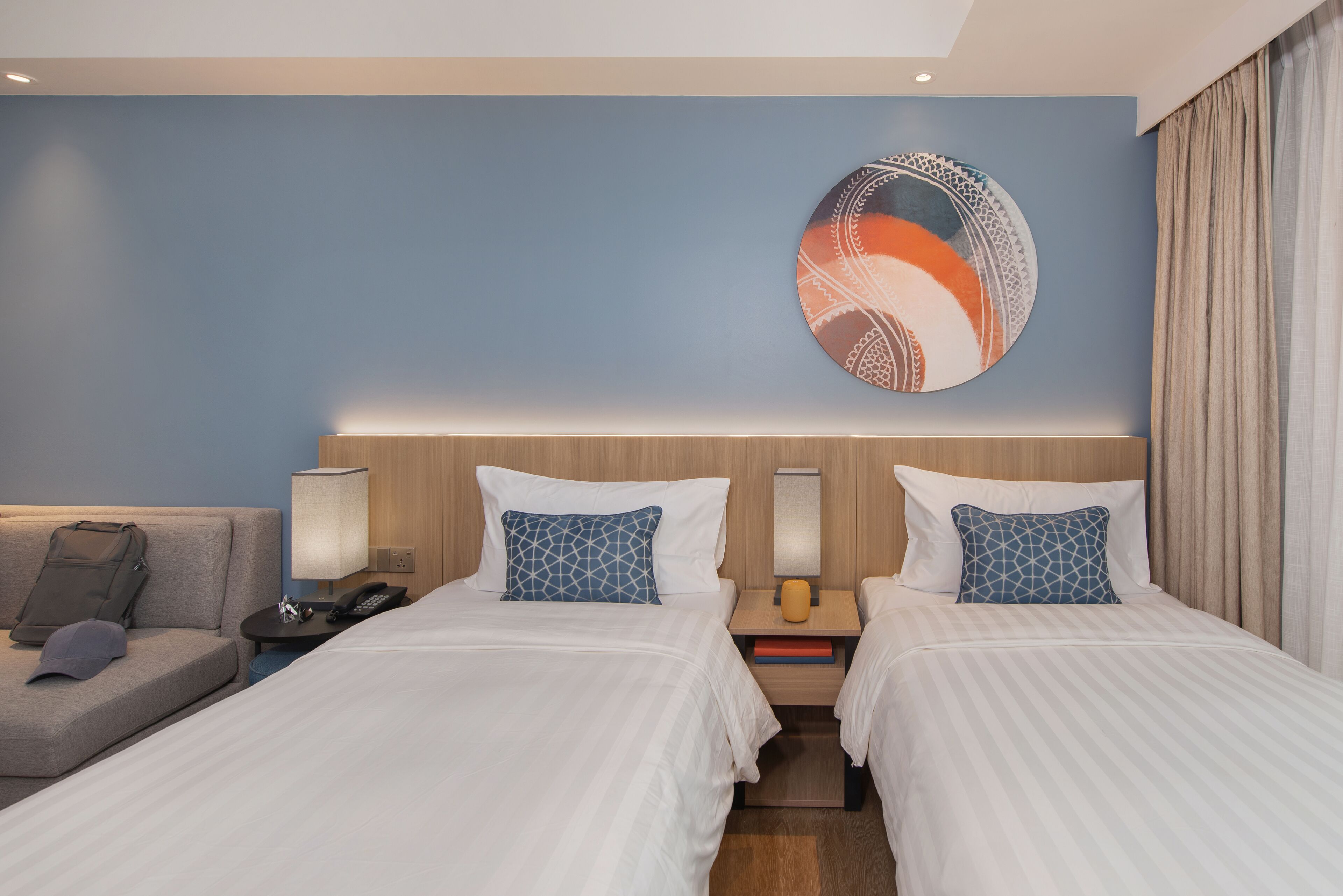 A hotel room with two beds, a sofa, a wall art piece, and a lamp.