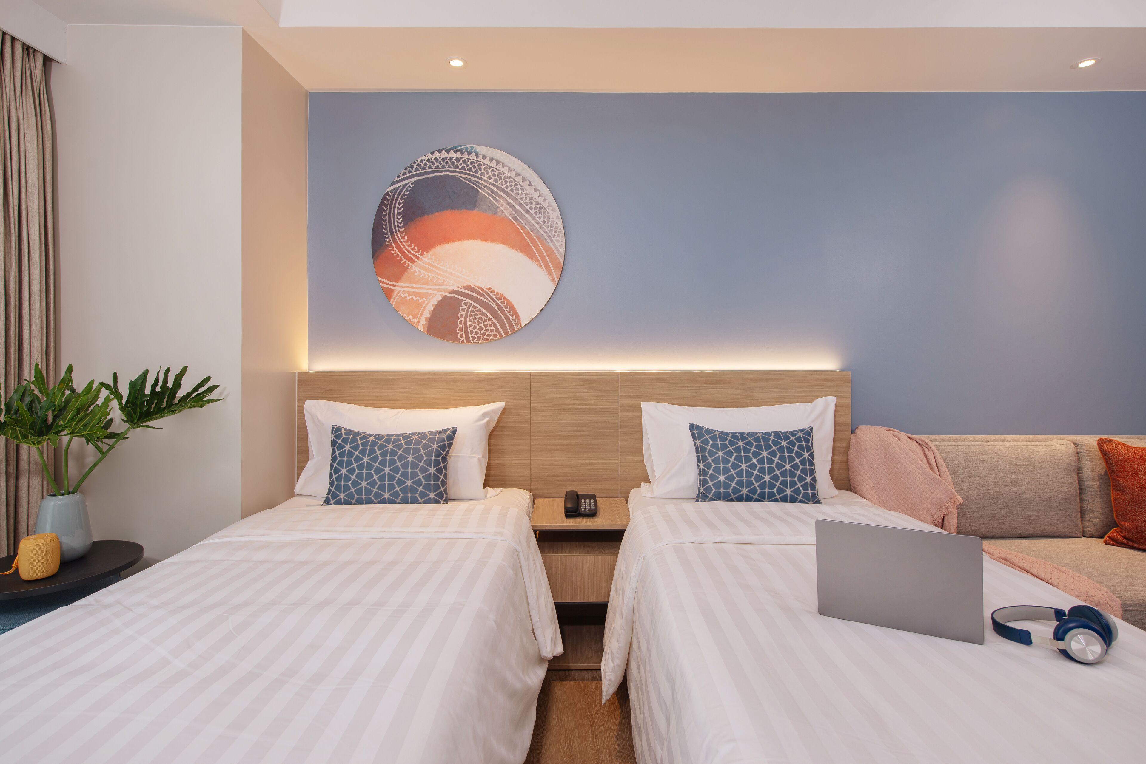 Habitación de hotel con dos camas, una laptop, audífonos y una obra de arte en la pared.