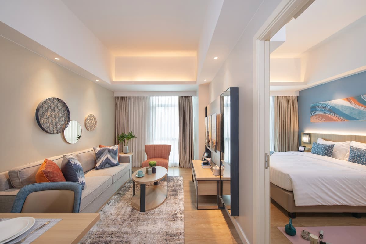 A modern hotel room with a sofa, a coffee table, a desk, and a bed.