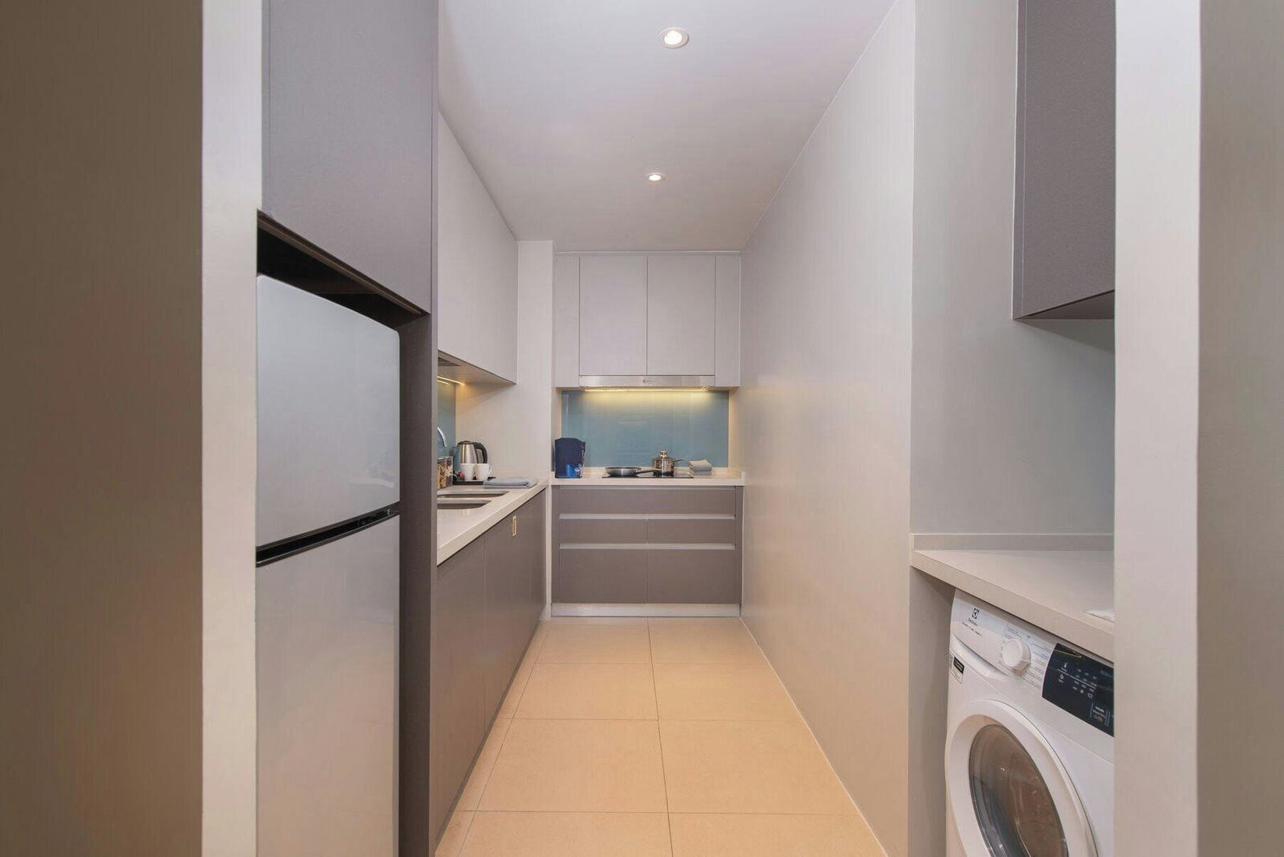 A narrow hallway with a washing machine, a kitchen area with a sink and cabinets, and a refrigerator.