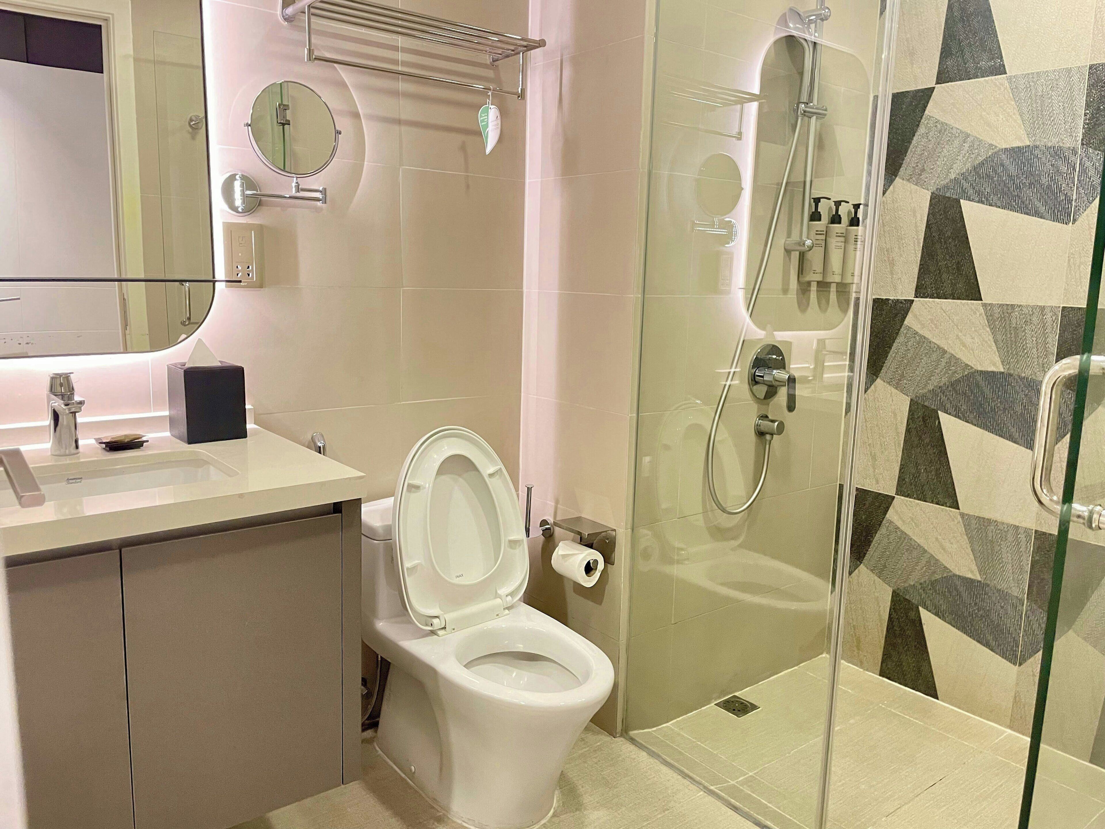 Een moderne badkamer met toilet, wastafel, spiegel en douche.