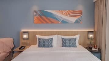 Una habitación de hotel con una cama grande, dos almohadas estampadas, una mesita de noche con teléfono y una obra de arte colgada en la pared.