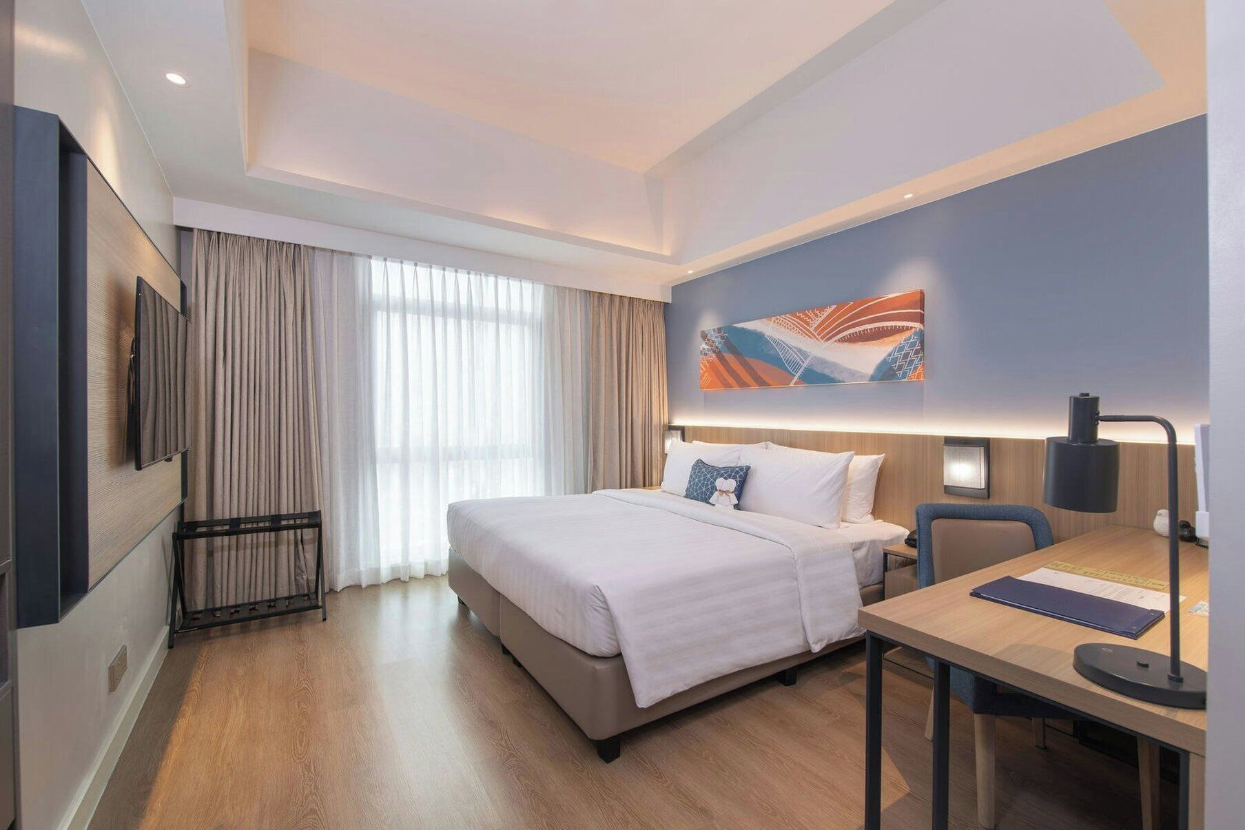 Una habitación de hotel con cama, escritorio, silla, televisor y un cuadro en la pared.