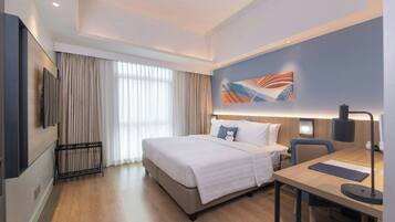 Una habitación de hotel con cama, escritorio, silla, televisor y un cuadro en la pared.