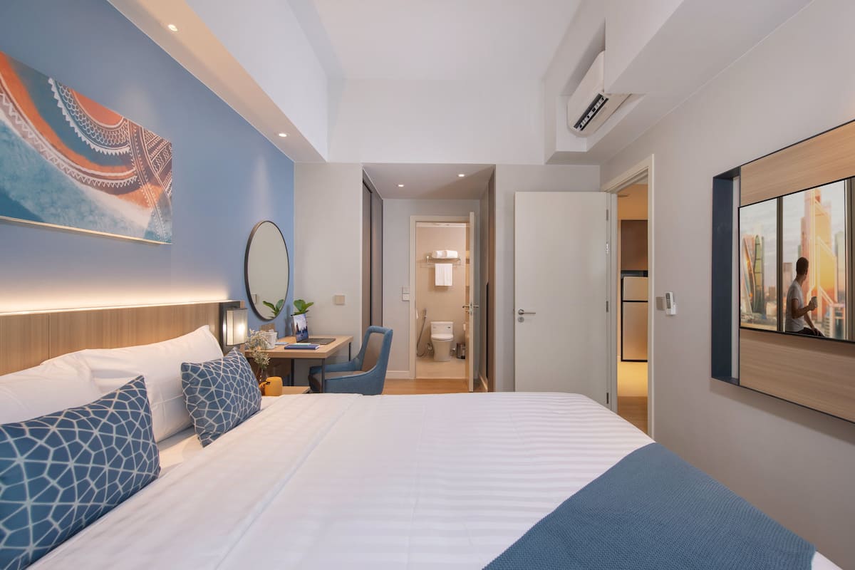 A hotel room with a large bed, a desk with a chair, a mirror, and a painting on the wall.