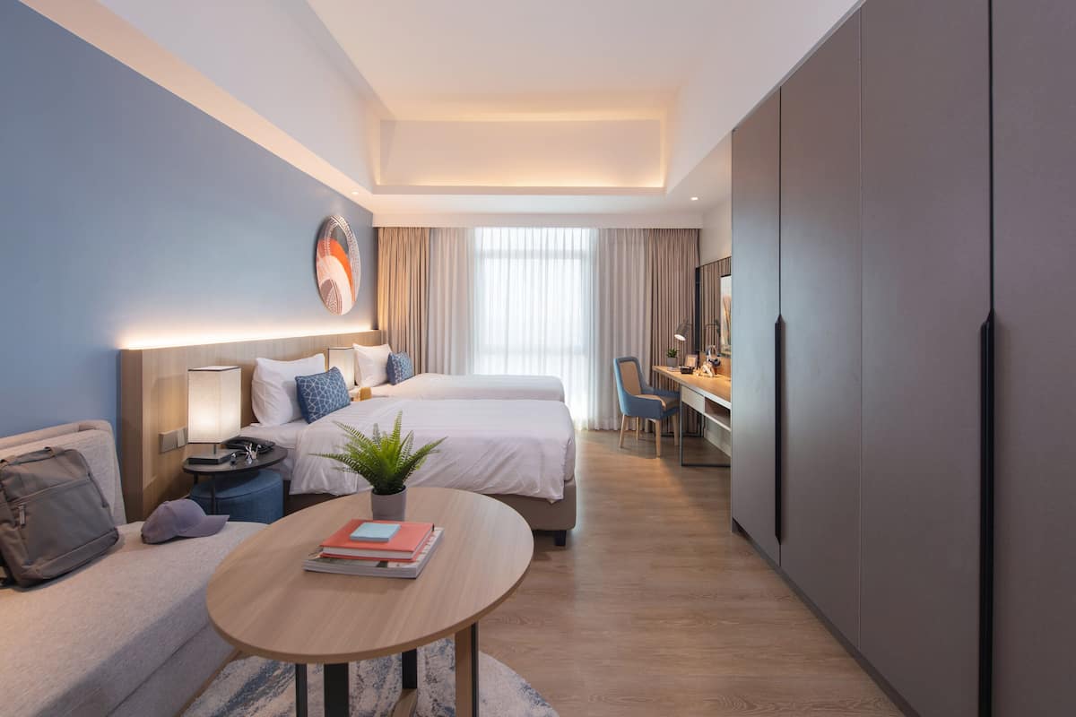 A modern hotel room with a bed, bedside table, lamp, and a desk with a chair.