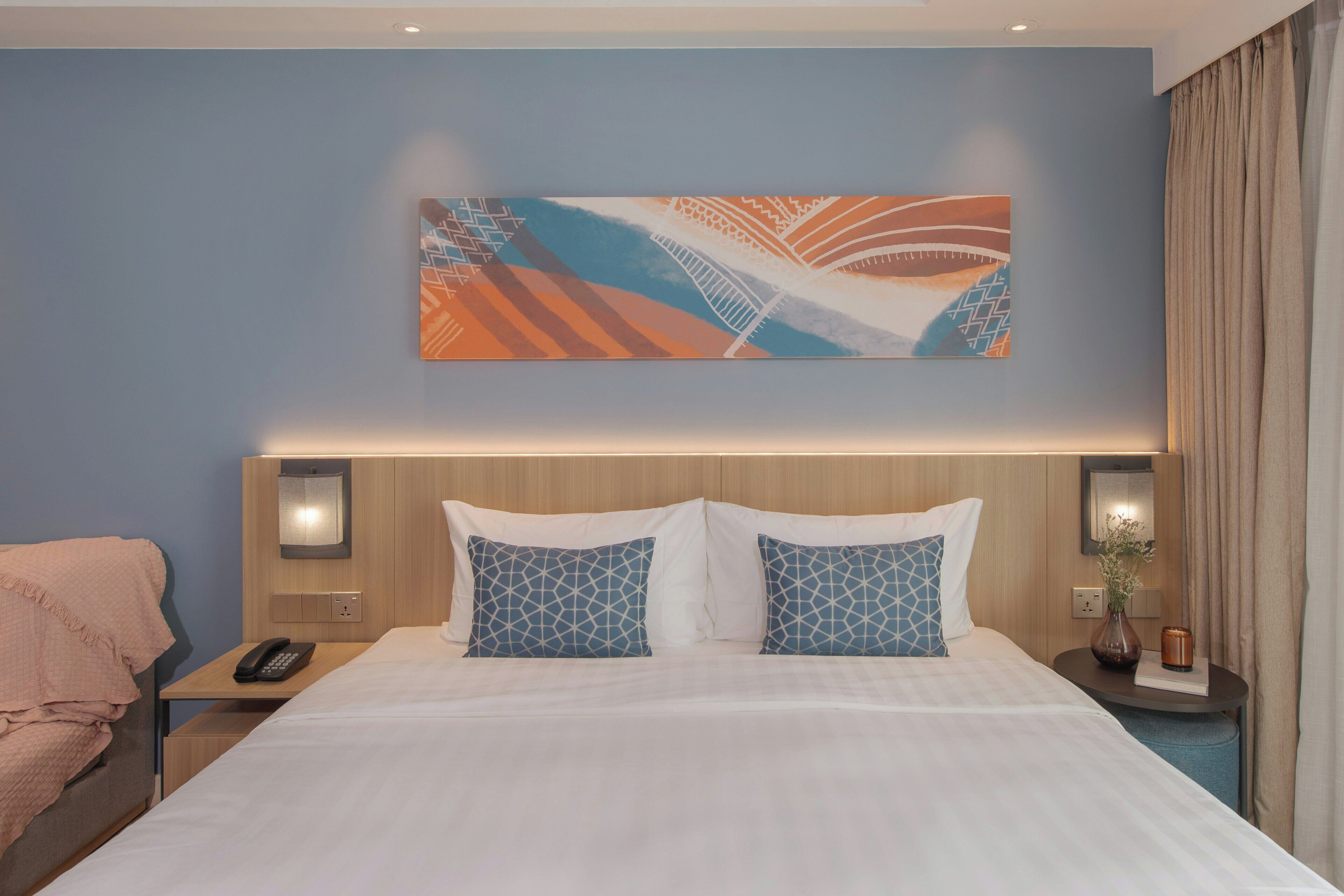 Habitación de hotel con una cama grande, dos mesitas de noche, un teléfono y una obra de arte colgada en la pared.