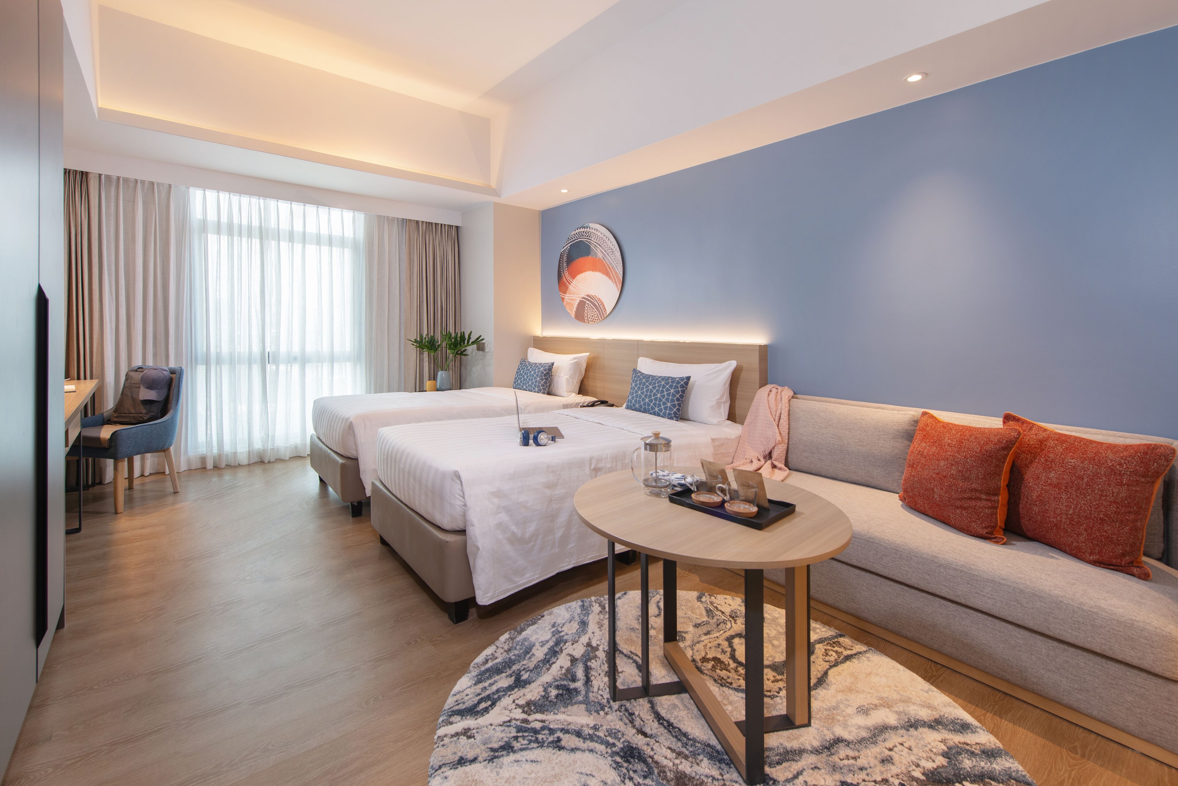 A modern hotel room with two beds, a sofa, a desk, and a coffee table.