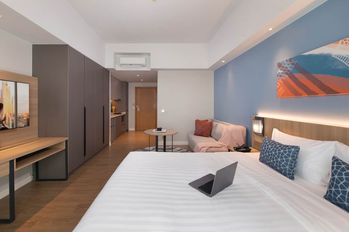 A modern hotel room with a large bed, a desk, a sofa, and a dining area.